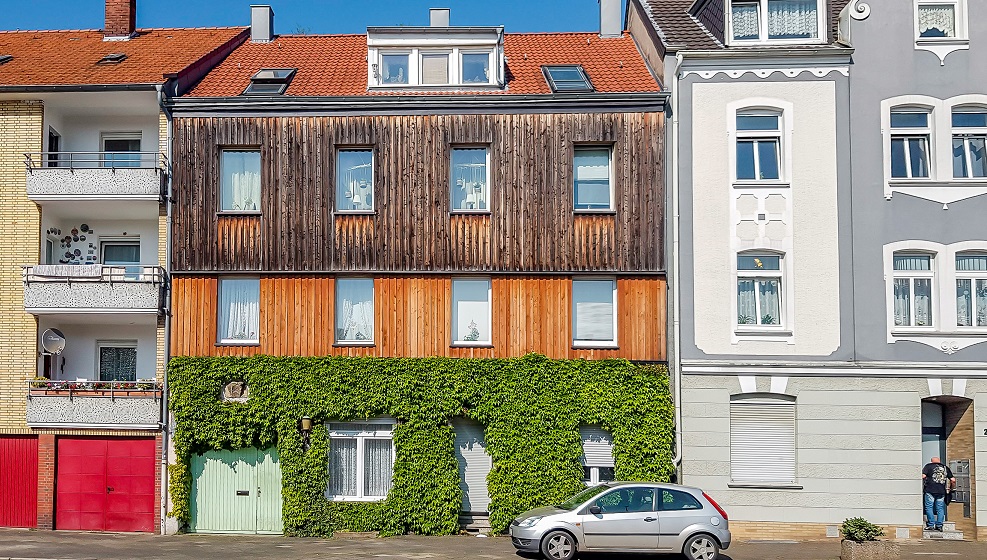 Mehrfamilienhaus in Häuserzeile mit Fassadenbegrünung im unteren Bereich