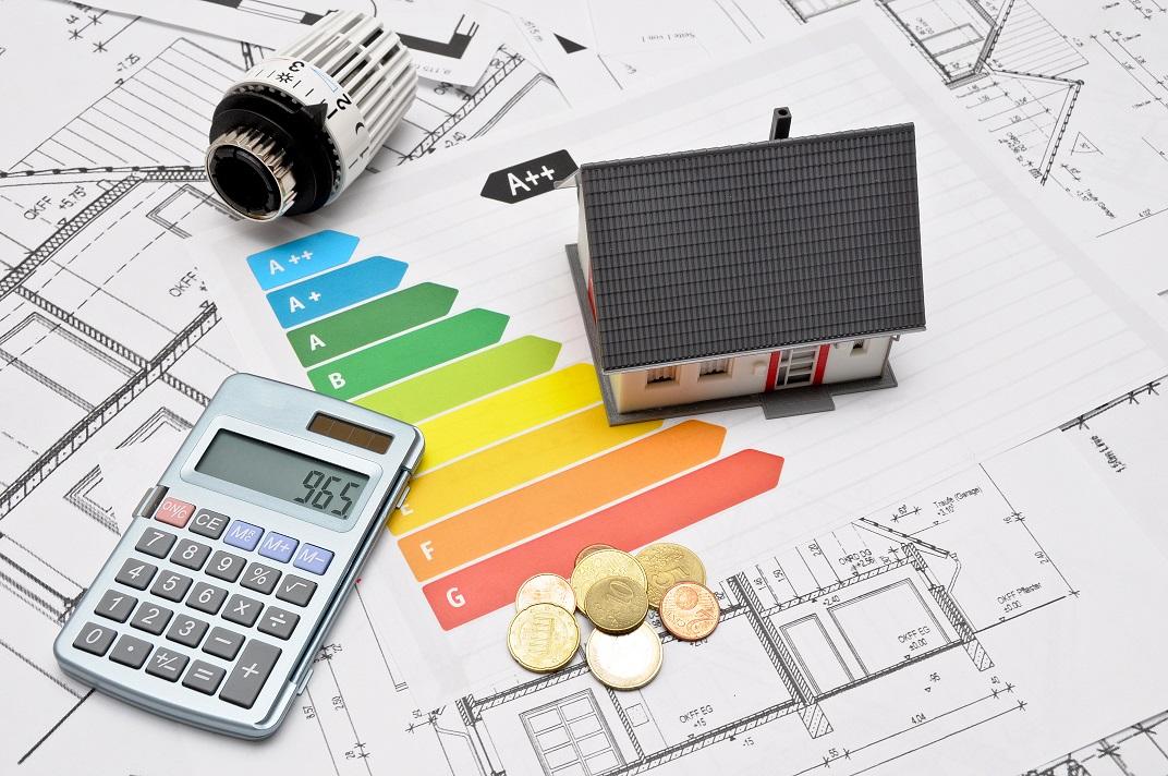 Bauplan mit Energieeffizienzskala, auf dem ein Häuschen und ein Taschenrechner stehen