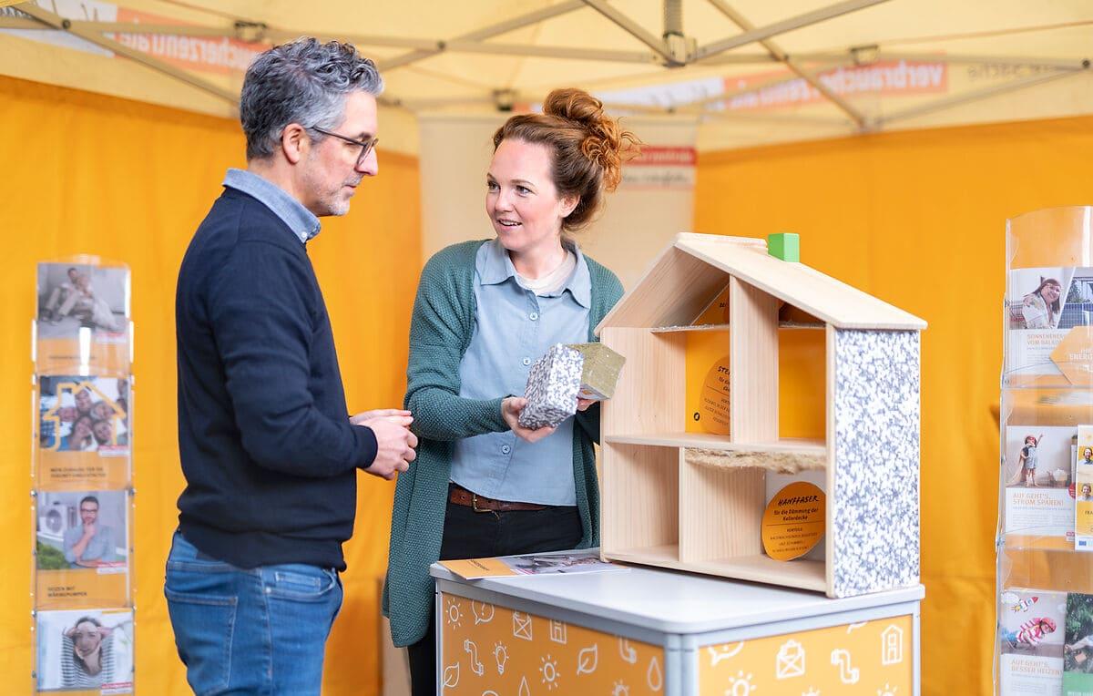 Beratungssituation vor einem Modellhaus mit verschiedenen Dämmstoffen