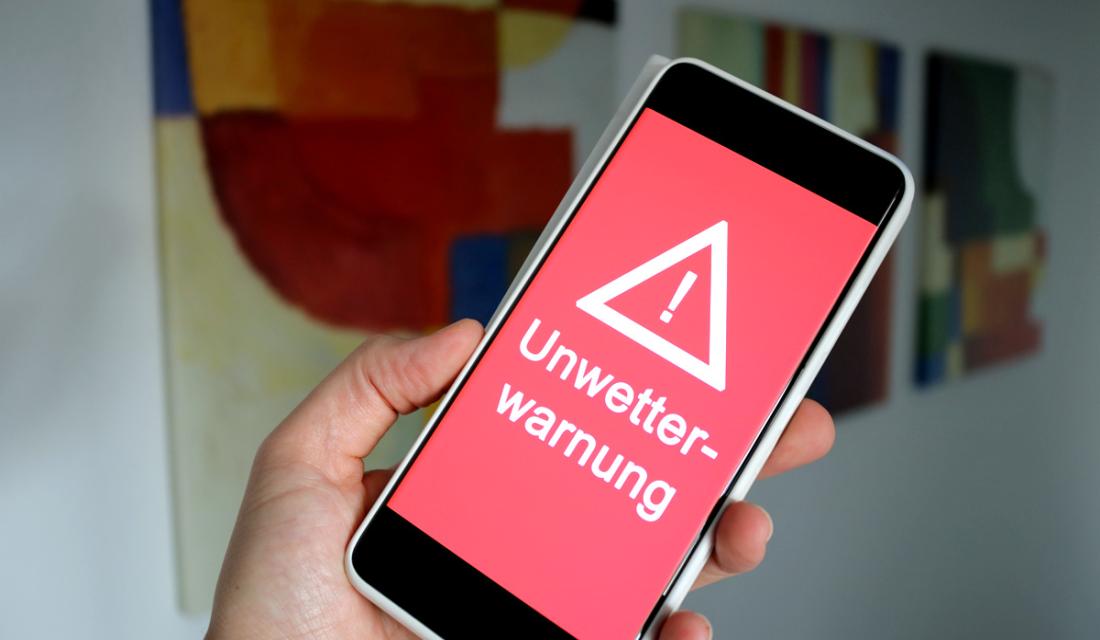 Smartphone mit rotem Display, Ausrufezeichen und dem Wort Unwetterwarnung