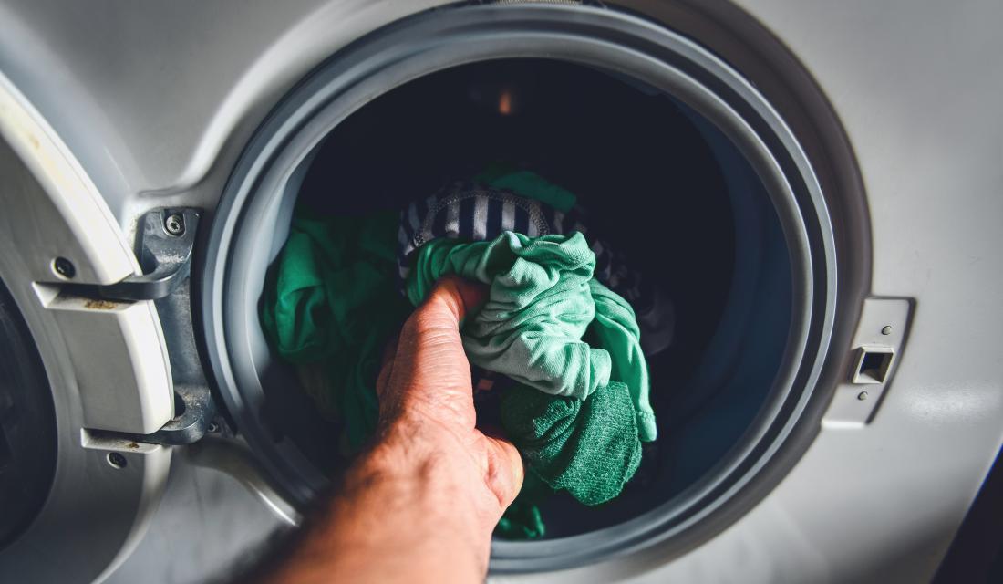 Hand greift in Waschmaschine nach Wäsche