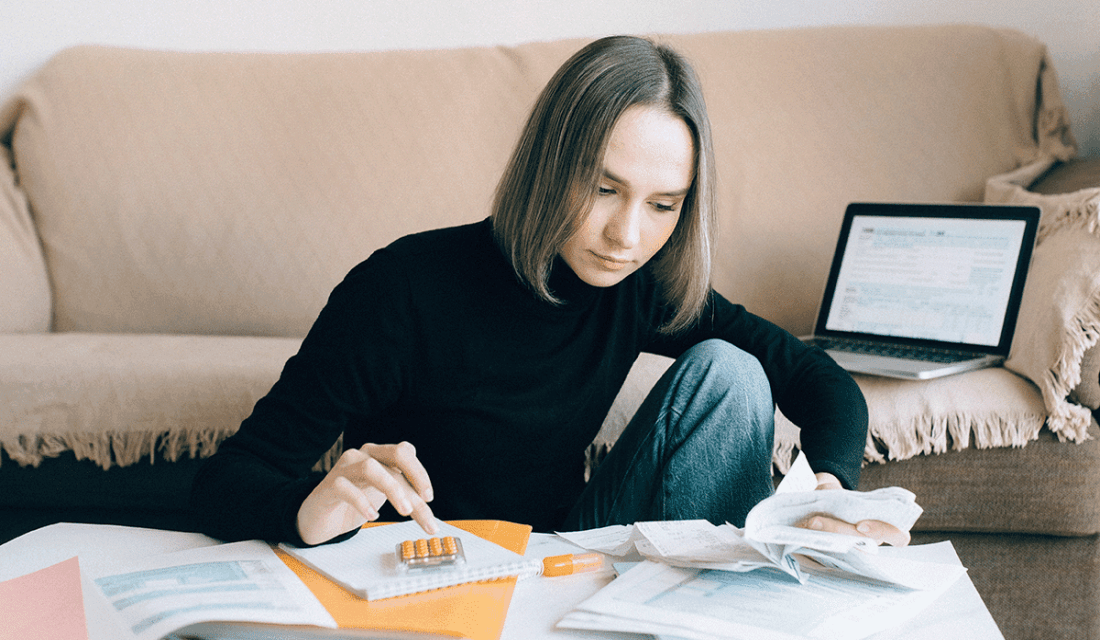 Junge Frau sitzt konzentriert an Tisch mit Unterlagen und Taschenrechner