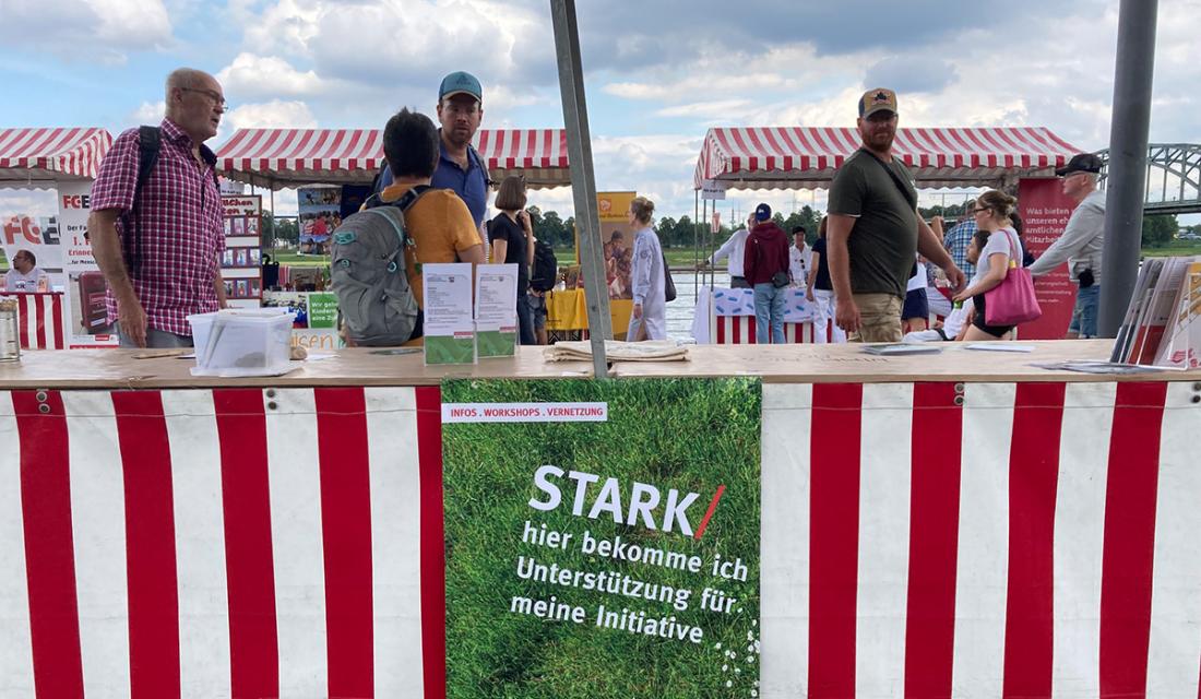 Menschen an einem Stand mit der Aufschrift "Stark - hier bekomme ich Unterstützung für meine Initiative"