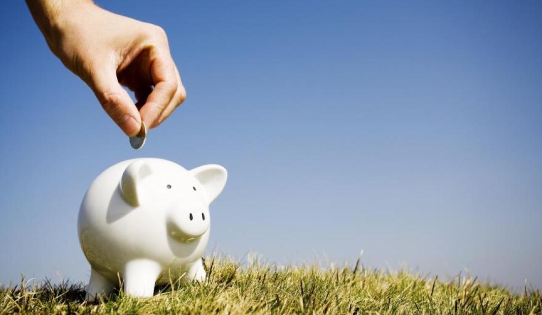 Hand wirft Geld in ein Sparschwein