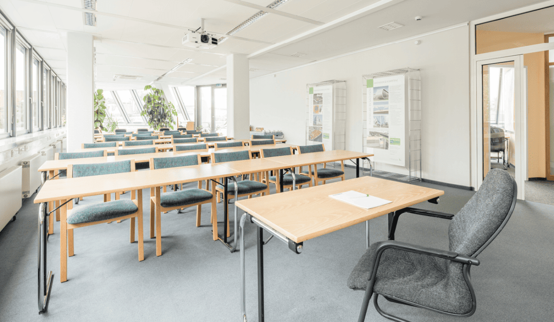 Vortragsraum mit Tischreihen und Stühlen, davor ein Pult und Stuhl für Referierende