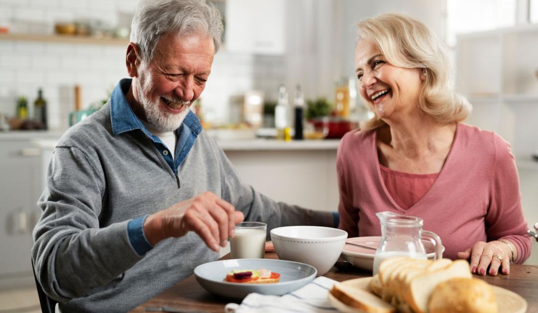 zwei ältere Personen sitzen lachend am Frühstückstisch
