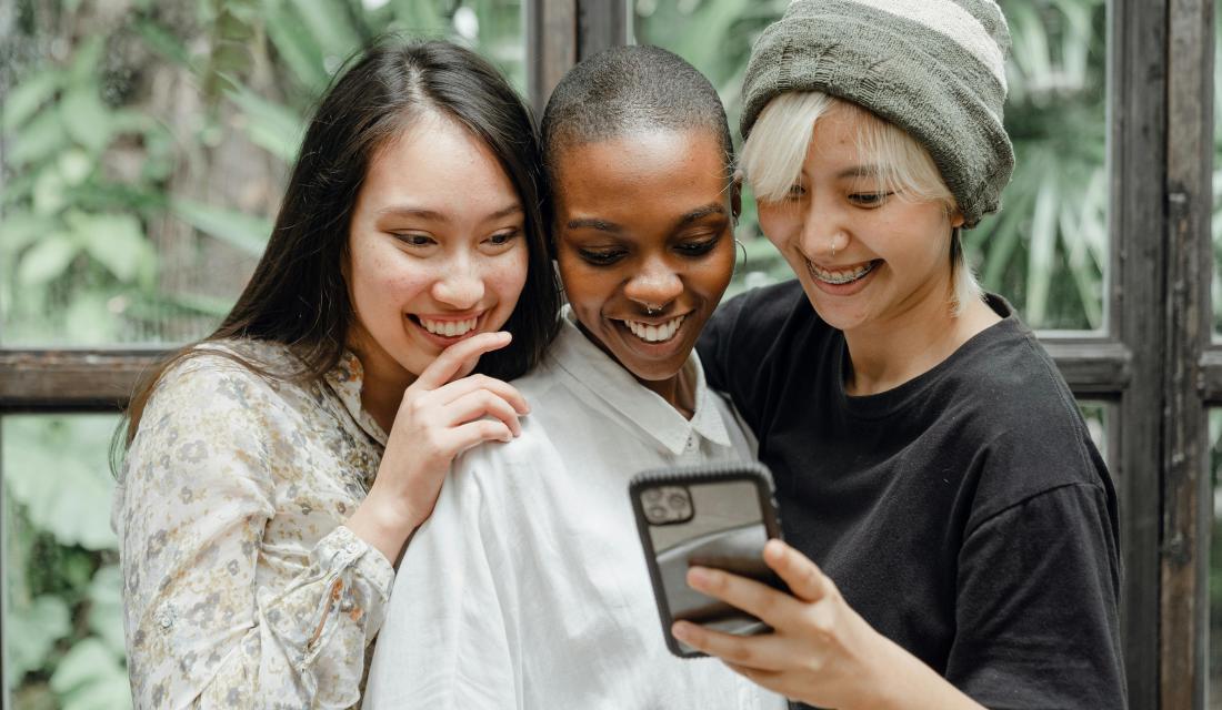 Drei Frauen, die lächelnd auf ein Smartphone schauen