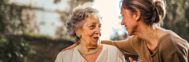 eine ältere und eine junge Frau sitzen im Garten und unterhalten sich