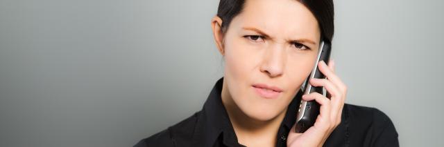 Eine Frau telefoniert und schaut dabei ernst.