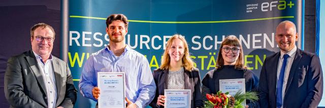 Fünf Personen stehen nebeneinander und lächeln in die Kamera