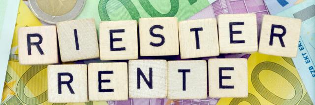 Scrabble-Steine, die das Wort Riester-Rente bilden, liegen auf Geldscheinen und Münzgeld