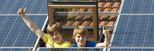 Kinder winken aus dem Dachfenster neben einer Photovoltaikanlage