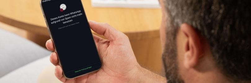 Ein Mann hält ein Smartphone in der Hand, auf dessen Disyplay in weißer Schrift auf schwarzem Hintergrund steht: "Dieses Konto kann WhatsApp aufgrund von Spam nicht mehr benutzen. Chats sind noch auf diesem Gerät."