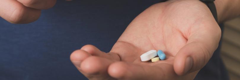 Eine Männerhand legt eine Tablette mit Nahrungsergänzungsmittel in die andere Hand, in der weitere Tabletten liegen