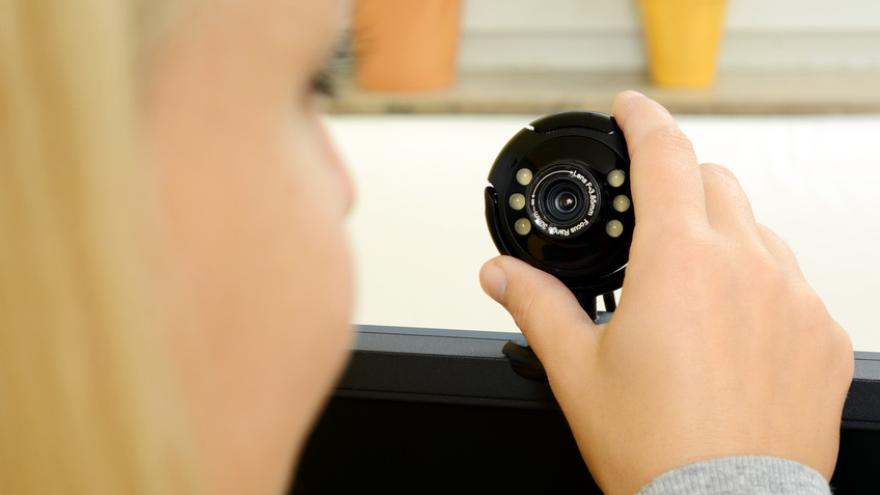 Blonde Frau hält ihre Hand an eine Webcam auf ihrem PC-Monitor