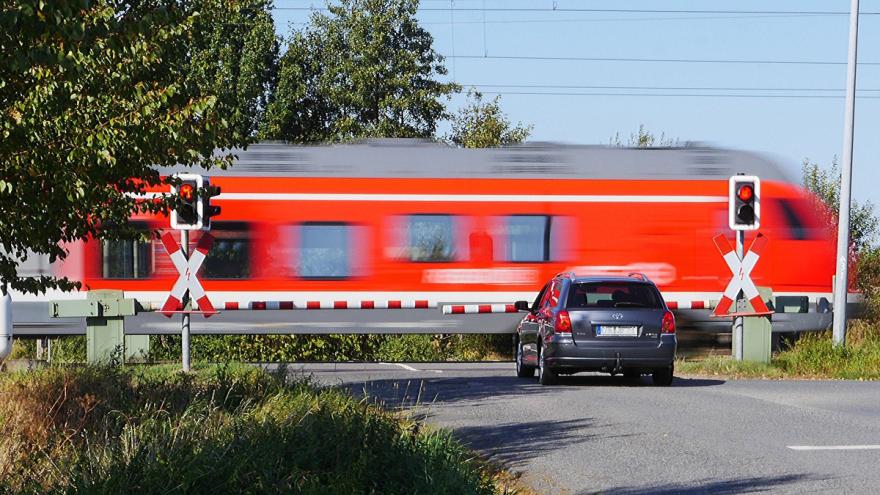 Auto am Bahnübergang vor vorbeifahrendem roten Zug.