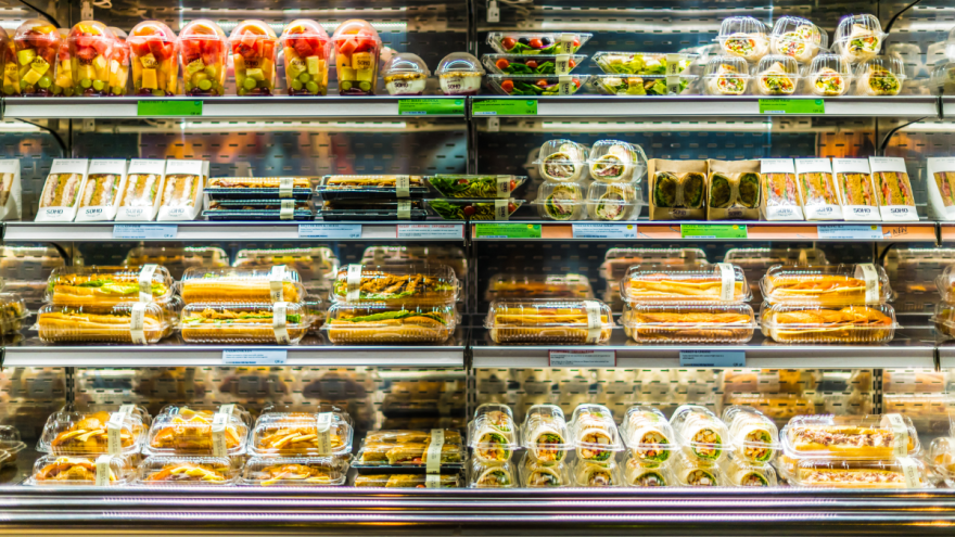 In einem Supermarktregal stehen zahlreiche Lebensmittel, die in Plastik verpackt sind.
