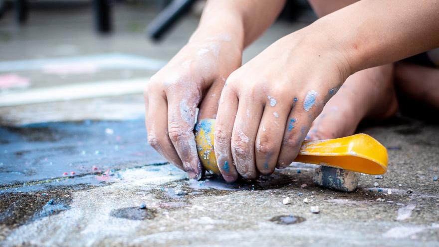 Kinderhände spielen mit Schaufel und Straßenmalkreide