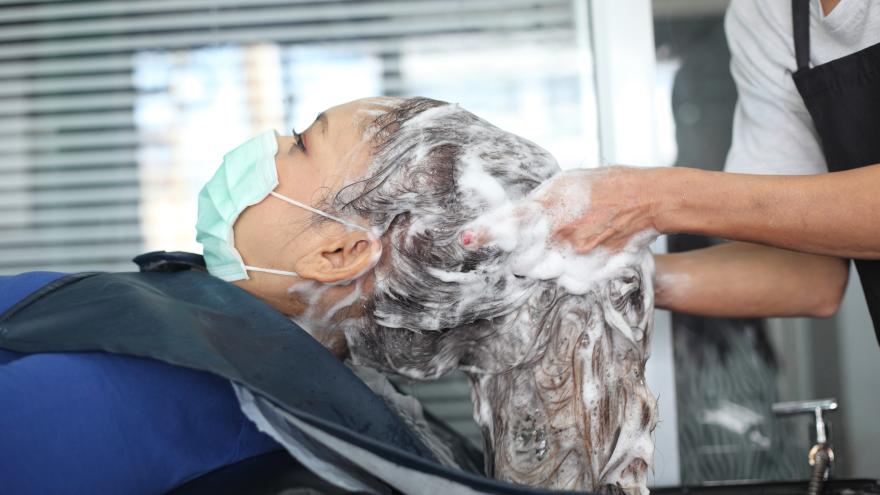 Frau mit Maske bekommt Haarwäsche beim Friseur