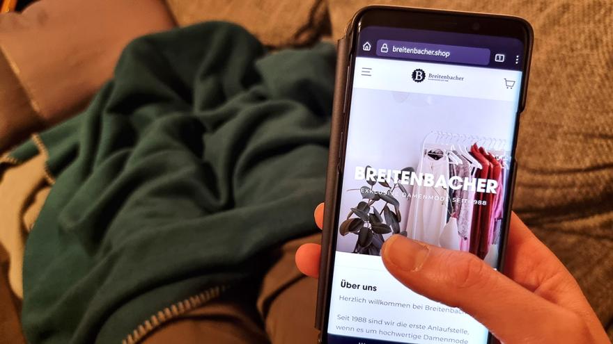 Person mit Smartphone auf einer Couch, auf dem Disyplay die Internetseite breitenbacher.shop