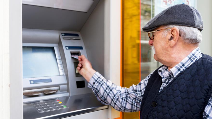 Ein älterer Mann steckt seine Geldkarte in einen Bankautomaten.