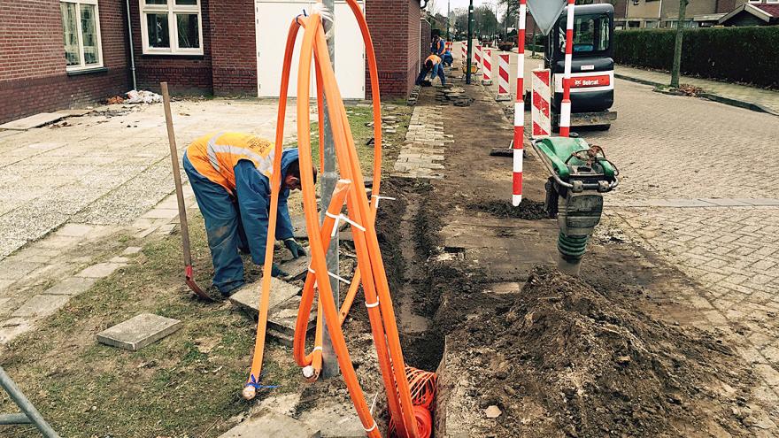 Baustelle: Männer legen orangefarbene Glasfaserkabel unter Gehwegplatten.