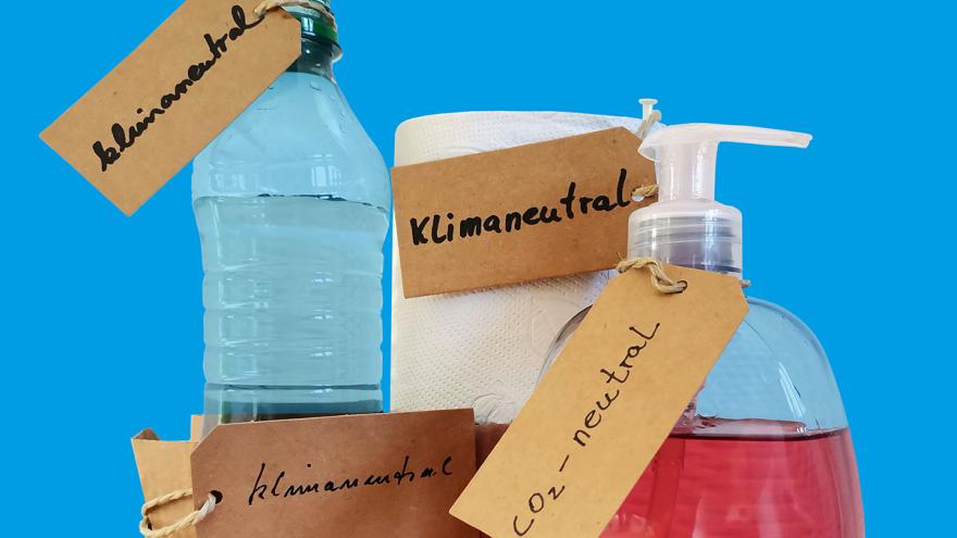 Wasserflasche, Küchenrolle und Seifenspender mit handschriftlich beschriebenen Etiketten "klimaneutral" und "CO2-neutral"