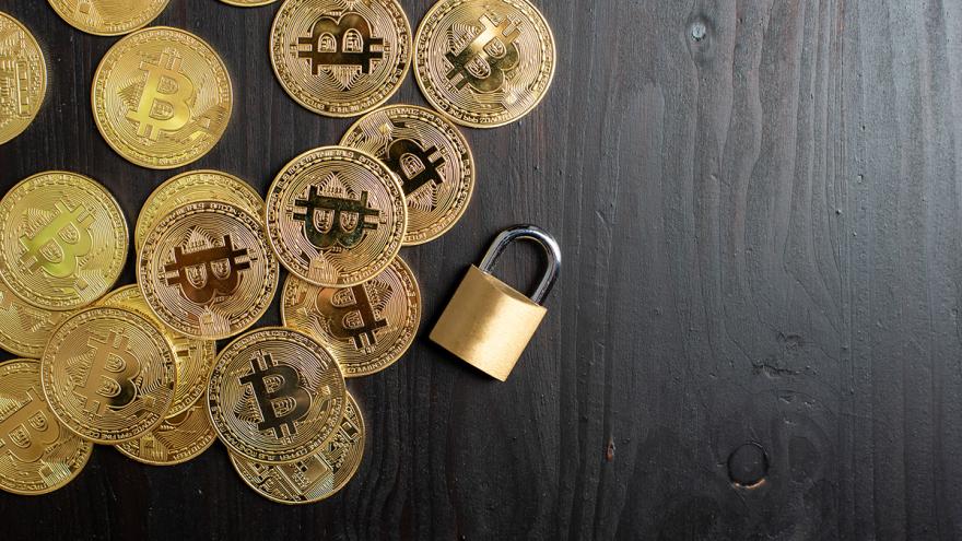 Bitcoin-Münzen und ein Vorhängeschloss auf schwarzer Tischplatte