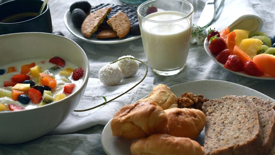 Frühstückstisch mit Müslischale, Milch, Brotkorb und Früchten