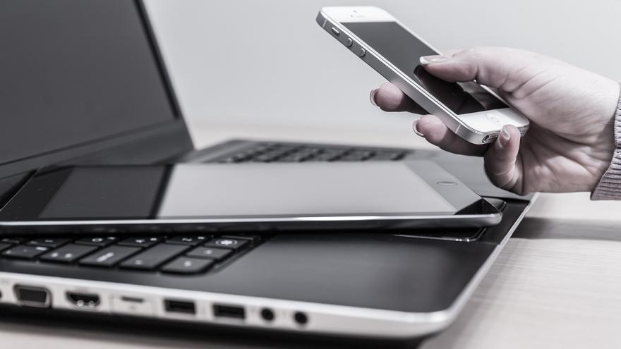 Hand hält Smartphone über Tablet und aufgeklapptem Laptop