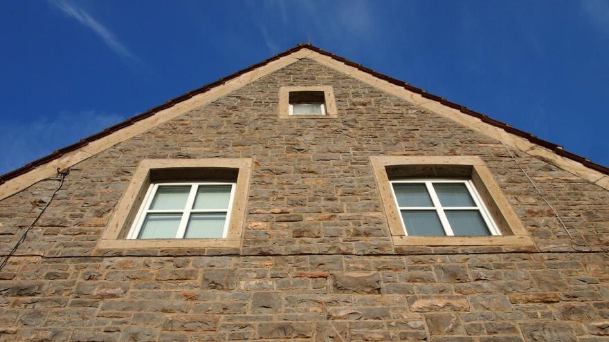 Hauswand und Giebel eines Steinhaus mit Fenstern und blauem Himmel