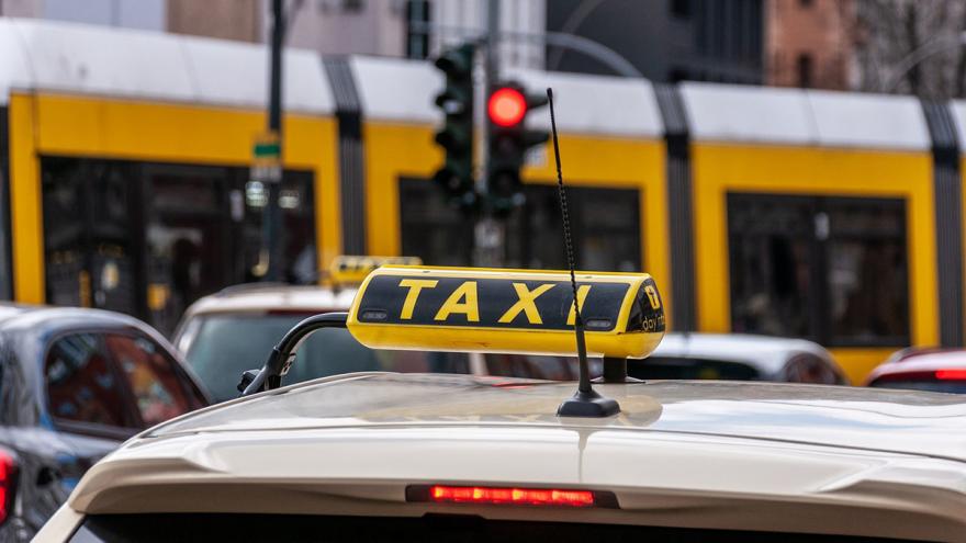 Ein Taxi steht an einer roten Ampel, hinter der eine Straßenbahn abbiegt.