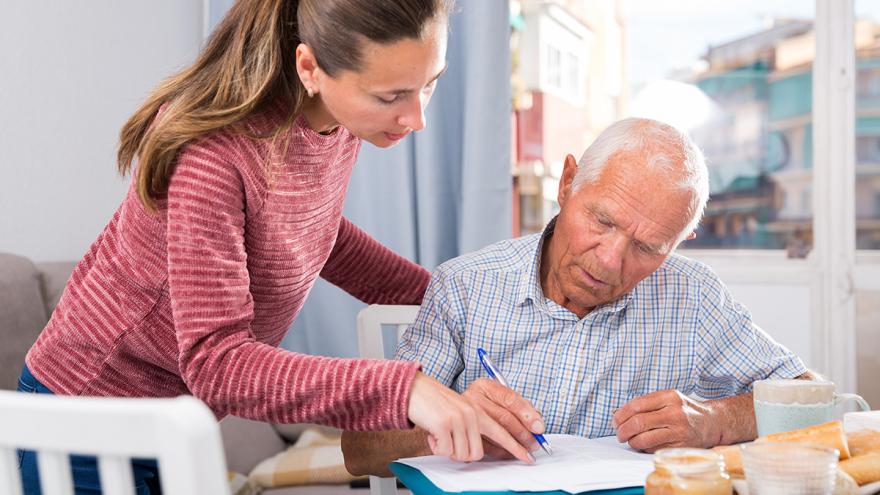 Eine Frau hilft einem Senior beim Ausfüllen von Dokumenten an einem Frühstückstisch