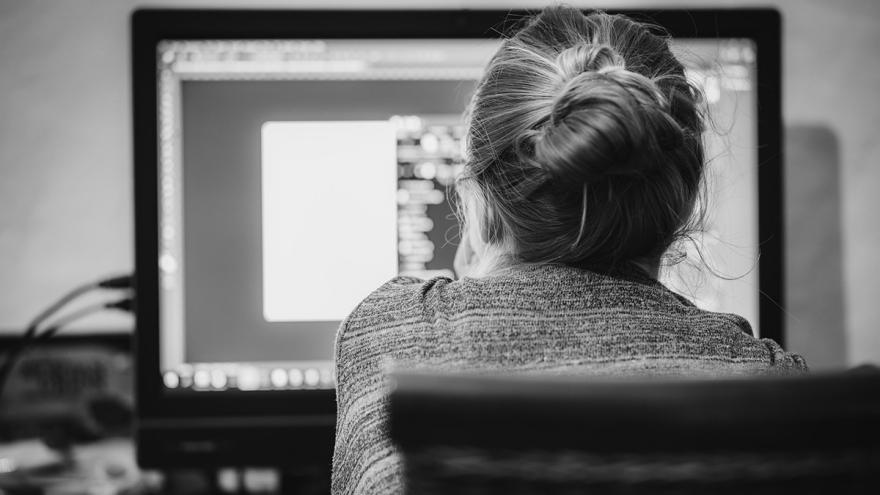 Eine Frau sitzt vor einem PC-Monitor, von hinten fotografiert