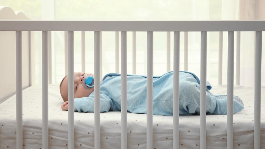 Baby in blauem Strampler schläft in weißem Bett