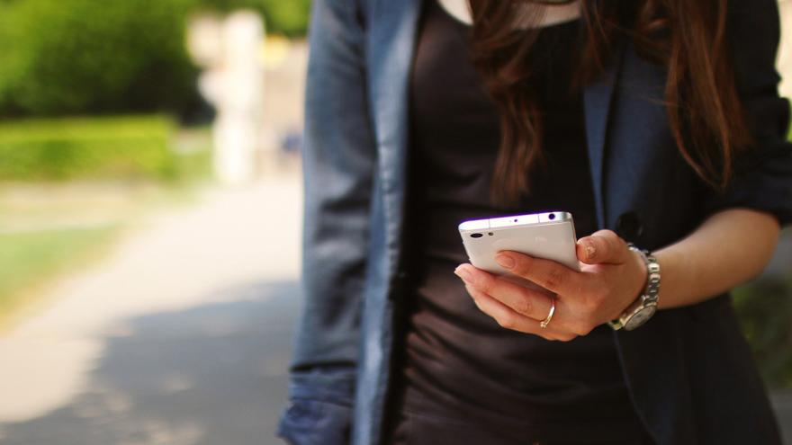 Frau geht mit einem Smartphone in ihrer Hand durch einen Park
