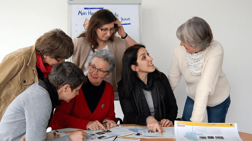 sechs Frauen sind um Tisch gruppiert und sehen sich Baupläne an