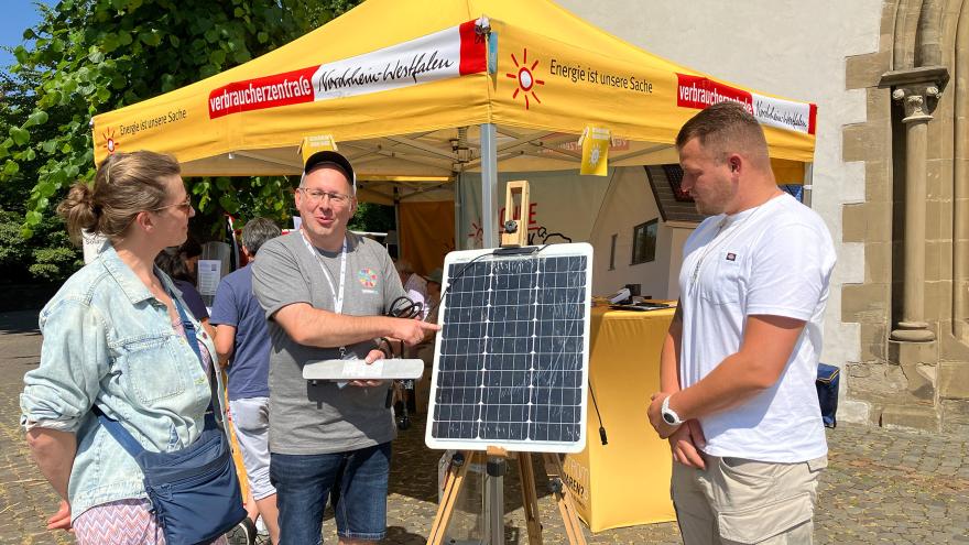 Infostand mit gelbem Sonnenschirm und 3 Personen