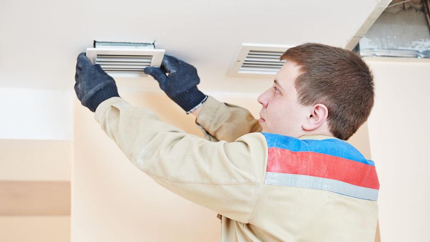 Installateur arbeitet an Lüftungsöffnung an einer Decke