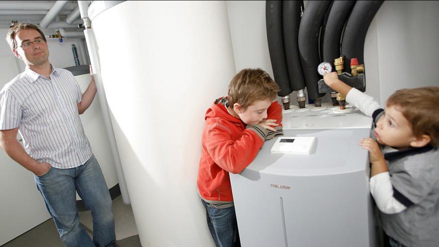 Mann und zwei Jungen sind im Heizungskeller und schauen sich die Wärmepumpe und den Wassertank an