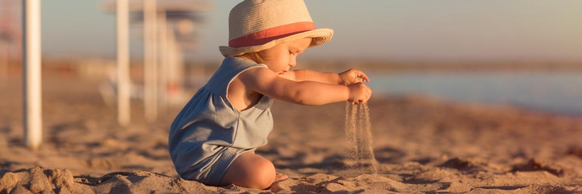 Ein Kind spielt am Strand im Sand und trägt einen Hut gegen die Sonne