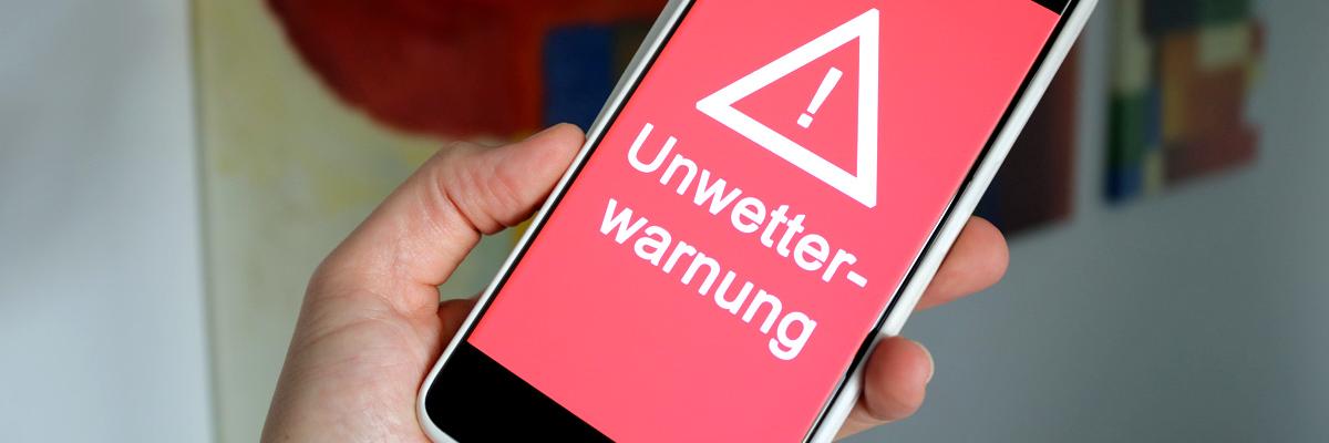 Smartphone mit rotem Display, Ausrufezeichen und dem Wort Unwetterwarnung
