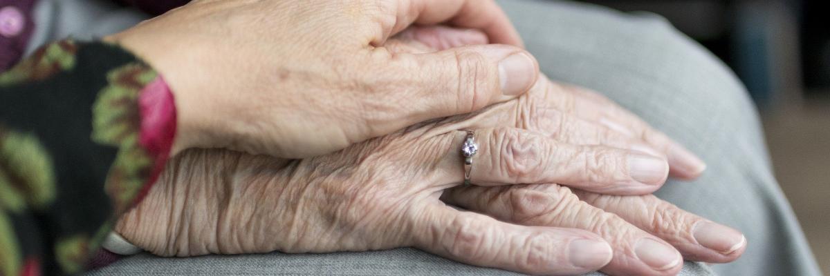 Eine jüngere Hand hält die Hand eines älteren Menschen.