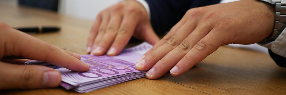 Hände schieben einen Stapel 500-Euro-Schein über einen Tisch