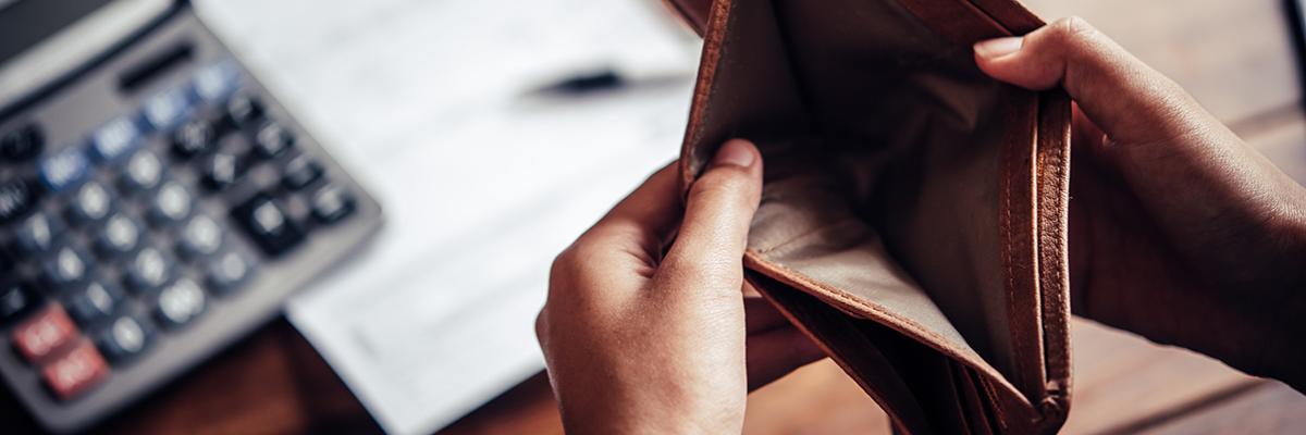 Zwei Hände halten ein leeres offenes Portmonee über einem Tisch mit Taschenrechner, Block und Stift