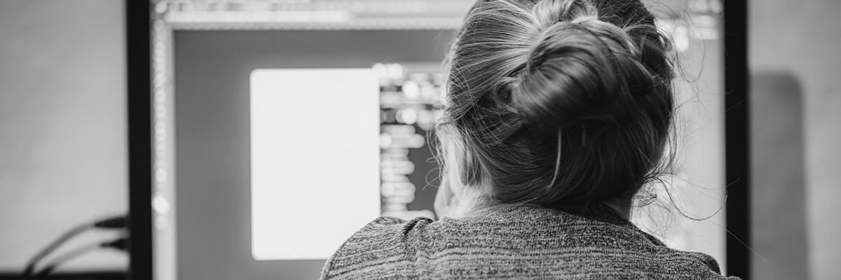 Eine Frau sitzt vor einem PC-Monitor, von hinten fotografiert