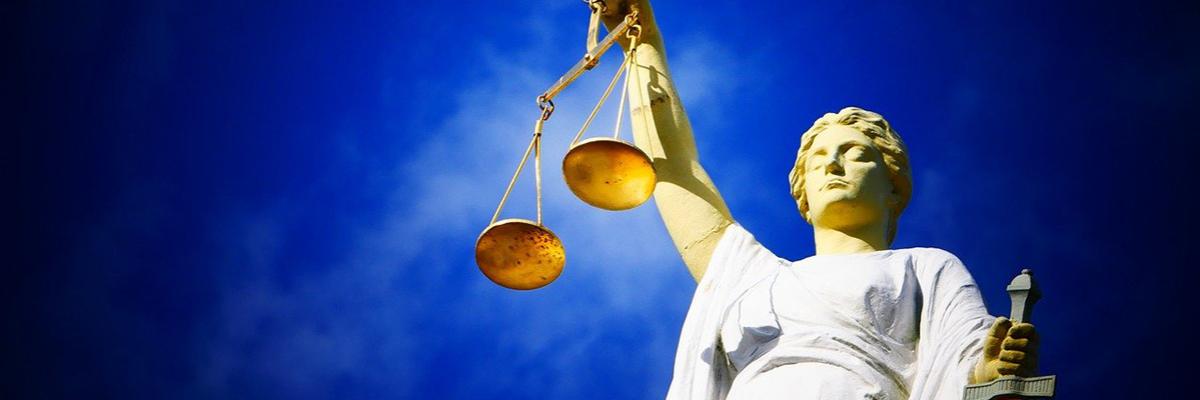 Statue der Justizia mit Waage und Schwert vor blauem Himmel