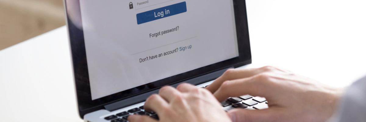 Zwei Hände auf einer Laptop-Tastatur, auf dem Bildschirm sind Eingabefelder zum Einloggen in ein Online-Konto zu sehen.