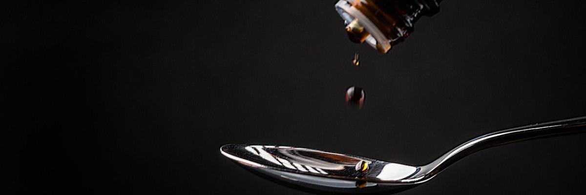 Tropfen aus einer kleinen Flasche fällt auf einen Löffel