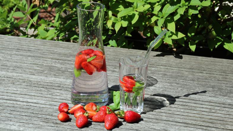 Karaffe und Glas gefüllt mit Wasser, Erdbeeren und Basilikum